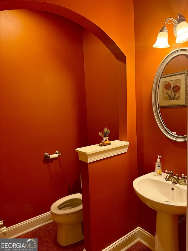 bathroom featuring baseboards, wood finished floors, and toilet