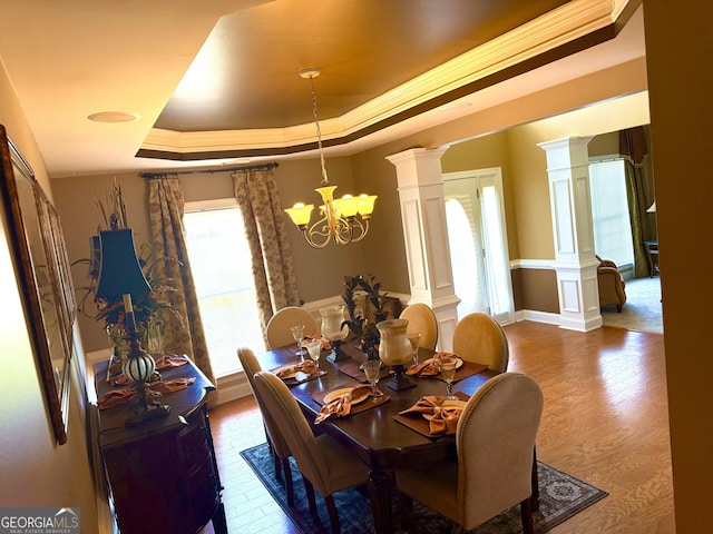 dining room featuring ornate columns, a tray ceiling, an inviting chandelier, and wood finished floors