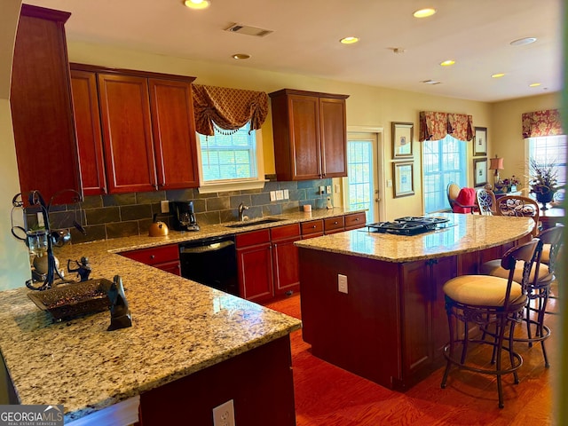 kitchen with visible vents, a kitchen island, black dishwasher, dark wood-style floors, and a sink
