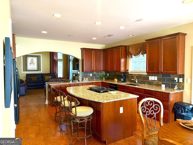 kitchen with decorative backsplash, wood finished floors, a kitchen island, a breakfast bar, and arched walkways