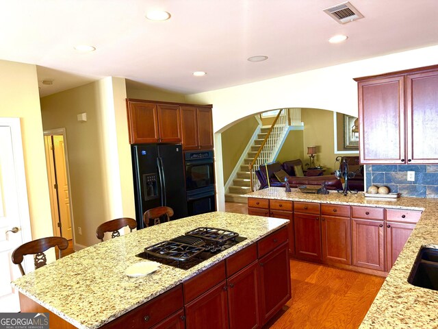kitchen with dark brown cabinets, arched walkways, light wood-type flooring, visible vents, and black appliances