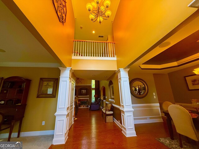 foyer entrance featuring crown molding, visible vents, wood finished floors, ornate columns, and a notable chandelier