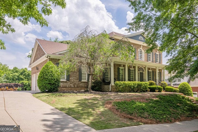 view of front of home with covered porch, driveway, a front yard, a garage, and brick siding