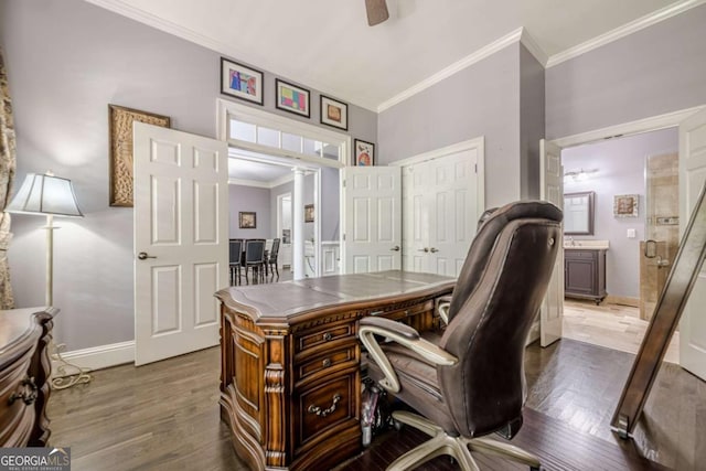 office space with crown molding, decorative columns, wood finished floors, baseboards, and ceiling fan