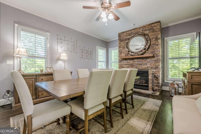 dining area featuring crown molding, ceiling fan, dark wood finished floors, and a stone fireplace