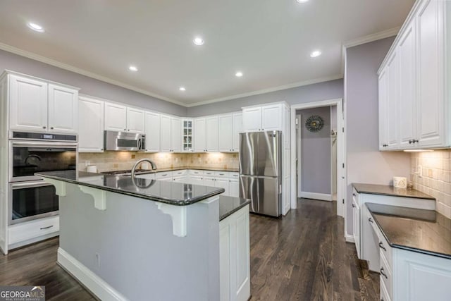kitchen with decorative backsplash, a breakfast bar, dark wood-type flooring, white cabinetry, and appliances with stainless steel finishes