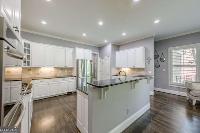 kitchen featuring freestanding refrigerator, dark countertops, a breakfast bar area, white cabinetry, and tasteful backsplash