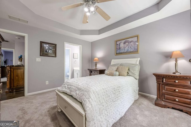 carpeted bedroom featuring connected bathroom, ceiling fan, baseboards, a tray ceiling, and visible vents