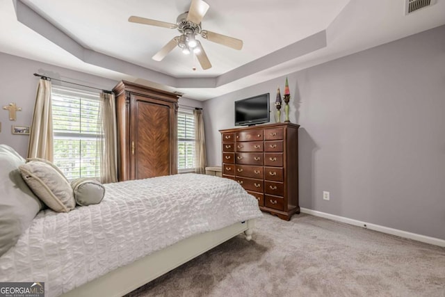 bedroom featuring light colored carpet, visible vents, multiple windows, and a raised ceiling