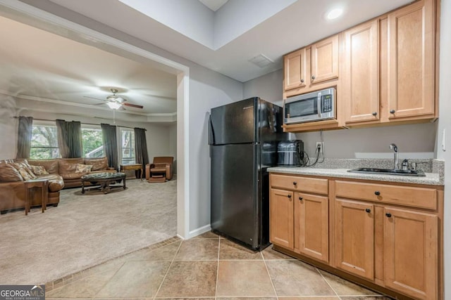 kitchen with a sink, light countertops, freestanding refrigerator, stainless steel microwave, and light carpet