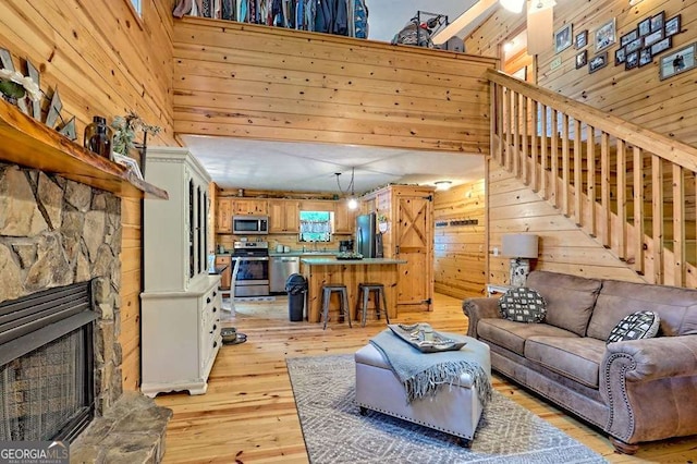 living area with a high ceiling, light wood-type flooring, wood walls, and a stone fireplace