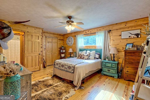 bedroom featuring a textured ceiling, wood walls, ceiling fan, and light wood-style floors