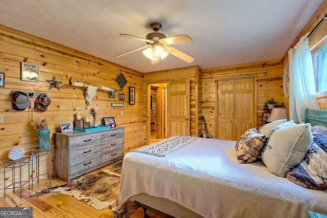 bedroom with a closet, a ceiling fan, wood walls, and wood finished floors