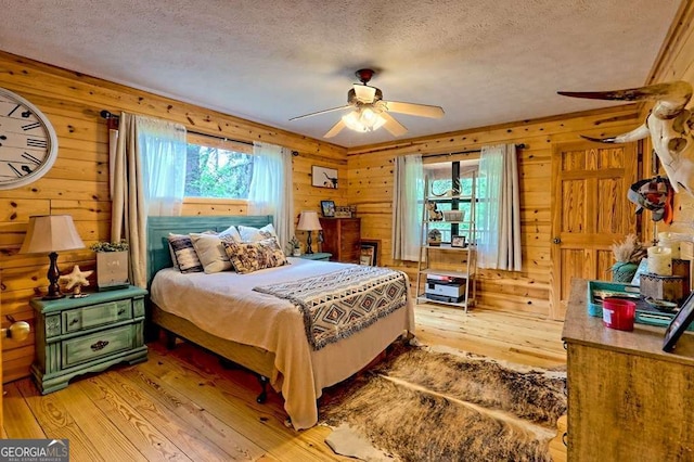 bedroom with multiple windows, light wood-style flooring, wood walls, and a textured ceiling