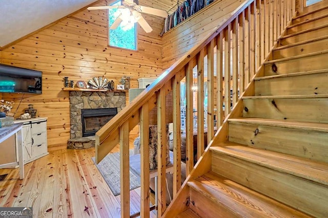 stairs featuring a ceiling fan, a fireplace, hardwood / wood-style flooring, lofted ceiling, and wooden walls