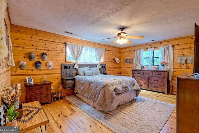bedroom with visible vents, a textured ceiling, light wood-style floors, and wooden walls