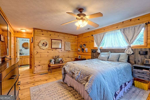 bedroom featuring light wood-type flooring, a ceiling fan, a textured ceiling, and wooden walls