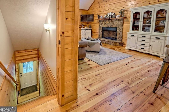 living area with light wood-style flooring, a fireplace, vaulted ceiling, and wooden walls