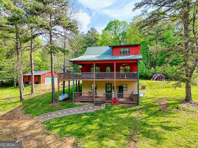 rear view of house with a lawn, a detached garage, an outbuilding, and metal roof