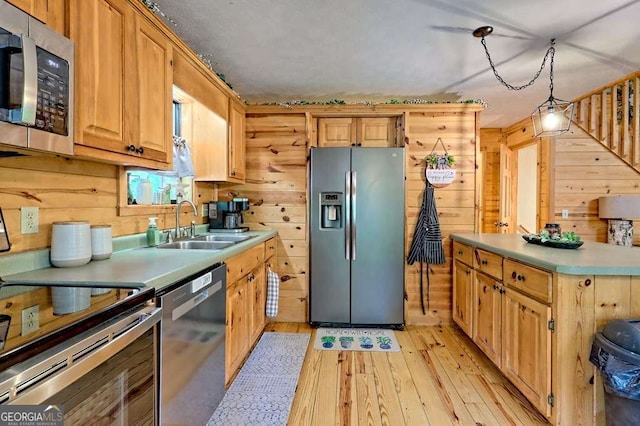 kitchen with wooden walls, appliances with stainless steel finishes, a sink, and light wood-type flooring