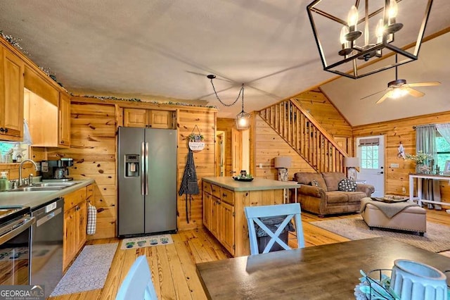 kitchen with wooden walls, a sink, light wood-style flooring, ceiling fan with notable chandelier, and stainless steel appliances