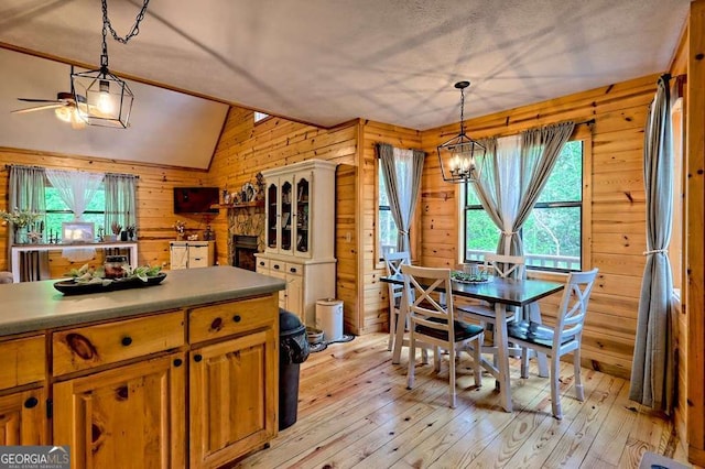 dining space with wooden walls, vaulted ceiling, light wood-type flooring, and ceiling fan with notable chandelier