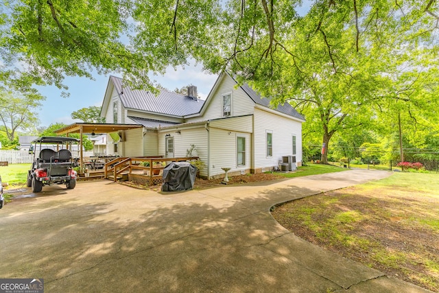 view of property exterior with concrete driveway, fence, metal roof, and a wooden deck