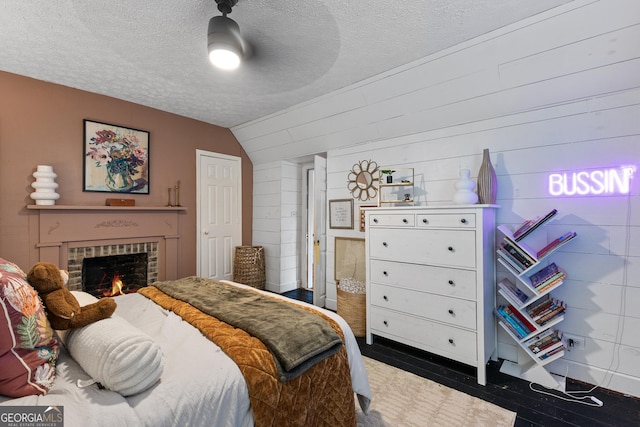 bedroom with wood walls, lofted ceiling, a fireplace, a textured ceiling, and a ceiling fan