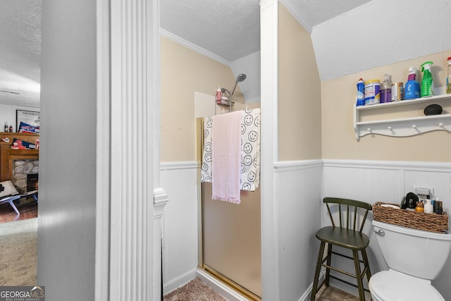 bathroom featuring a textured ceiling, a stall shower, toilet, and a wainscoted wall