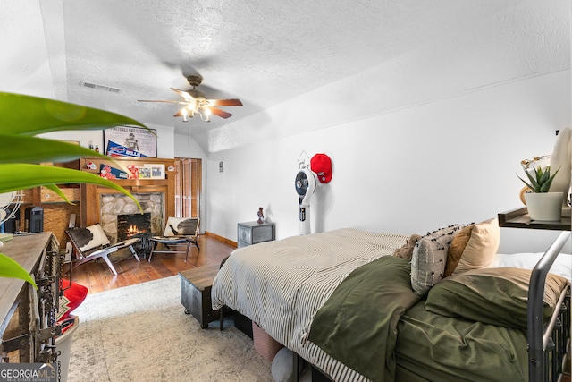 bedroom with a ceiling fan, a textured ceiling, visible vents, wood finished floors, and lofted ceiling