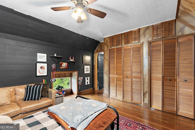 living area with ceiling fan, a textured ceiling, wood walls, wood finished floors, and vaulted ceiling