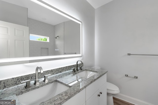 bathroom with a tile shower, toilet, double vanity, baseboards, and wood finished floors