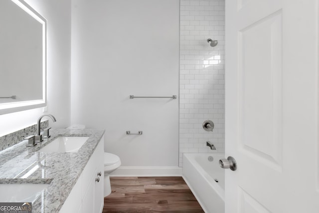 full bath with toilet, wood finished floors, double vanity, baseboards, and shower / bathtub combination