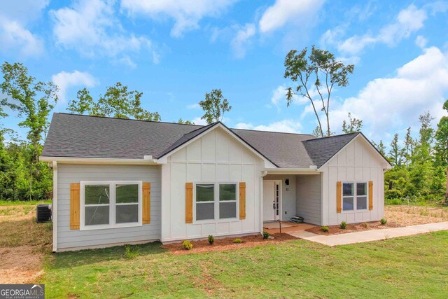 modern inspired farmhouse with board and batten siding, a front lawn, a shingled roof, and central AC unit