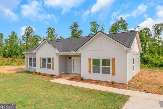 modern farmhouse with board and batten siding, a shingled roof, and a front yard