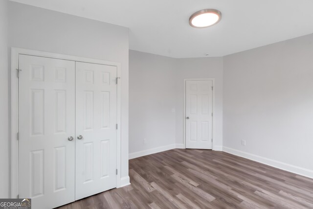 unfurnished bedroom featuring wood finished floors, baseboards, and a closet