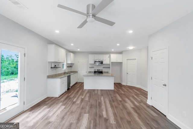 kitchen featuring stainless steel appliances, a sink, decorative backsplash, light wood-style floors, and baseboards