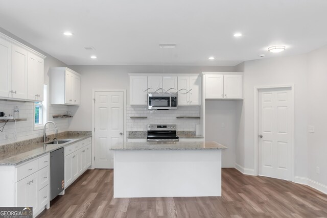 kitchen featuring appliances with stainless steel finishes, a sink, backsplash, wood finished floors, and recessed lighting