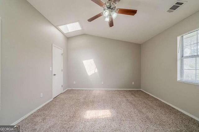 unfurnished room with visible vents, carpet floors, a ceiling fan, lofted ceiling with skylight, and baseboards
