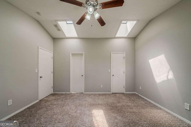 empty room with carpet, vaulted ceiling with skylight, visible vents, baseboards, and ceiling fan