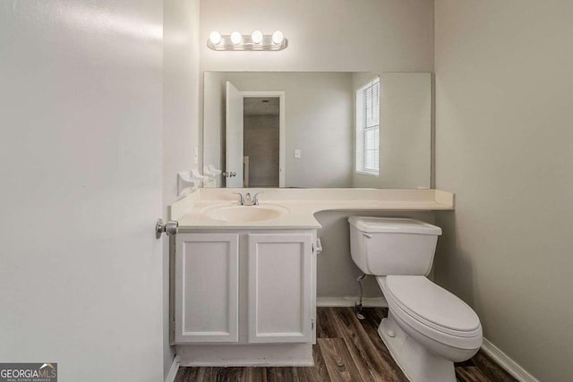 half bathroom featuring toilet, baseboards, wood finished floors, and vanity
