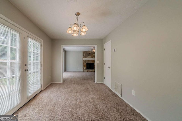 unfurnished dining area with a notable chandelier, baseboards, visible vents, a fireplace, and light colored carpet