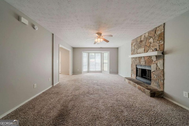 unfurnished living room with carpet floors, a textured ceiling, baseboards, a stone fireplace, and ceiling fan