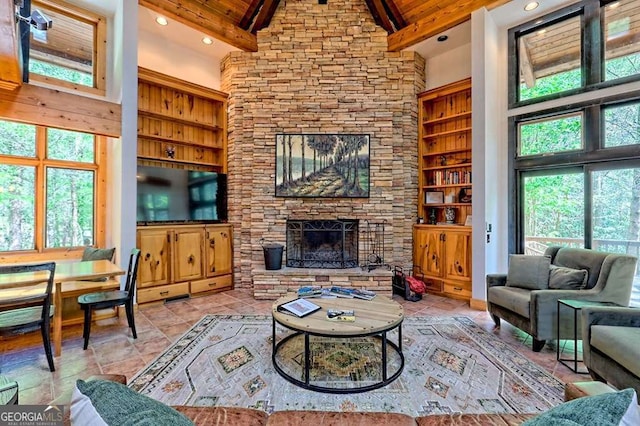 living area featuring beamed ceiling, high vaulted ceiling, a stone fireplace, and a healthy amount of sunlight
