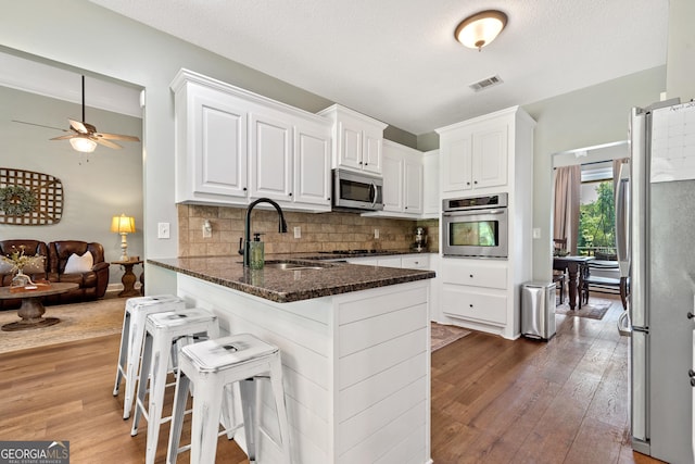 kitchen featuring stainless steel appliances, a sink, light wood-type flooring, tasteful backsplash, and white cabinets