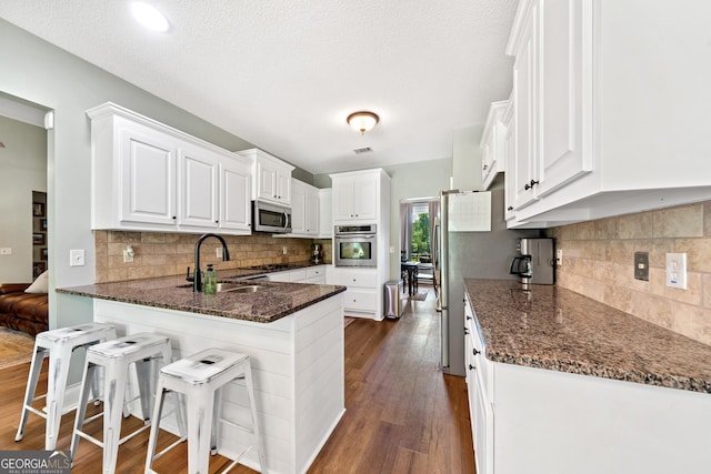 kitchen featuring appliances with stainless steel finishes, a sink, dark wood-style floors, and a peninsula