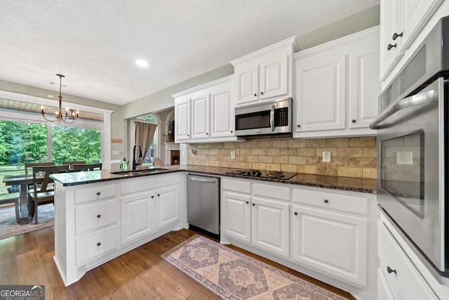 kitchen with appliances with stainless steel finishes, a sink, a peninsula, white cabinets, and a chandelier
