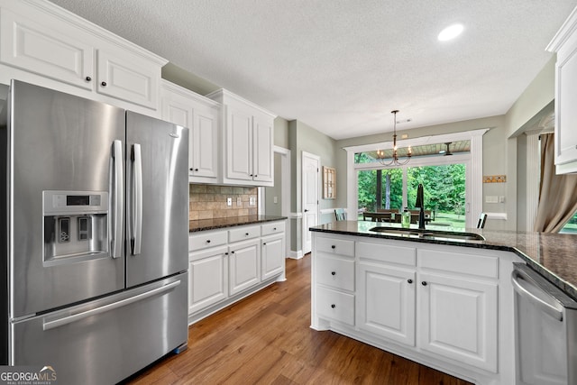 kitchen featuring appliances with stainless steel finishes, a sink, white cabinetry, wood finished floors, and a textured ceiling