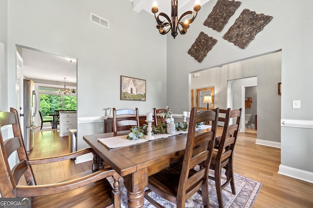 dining space featuring a chandelier, light wood finished floors, a towering ceiling, and baseboards