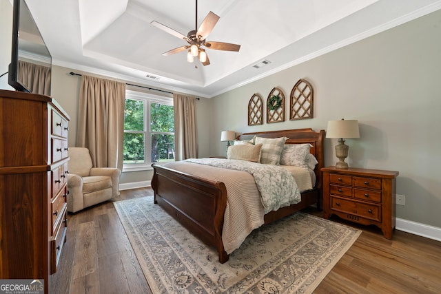 bedroom featuring a tray ceiling, hardwood / wood-style flooring, baseboards, crown molding, and ceiling fan